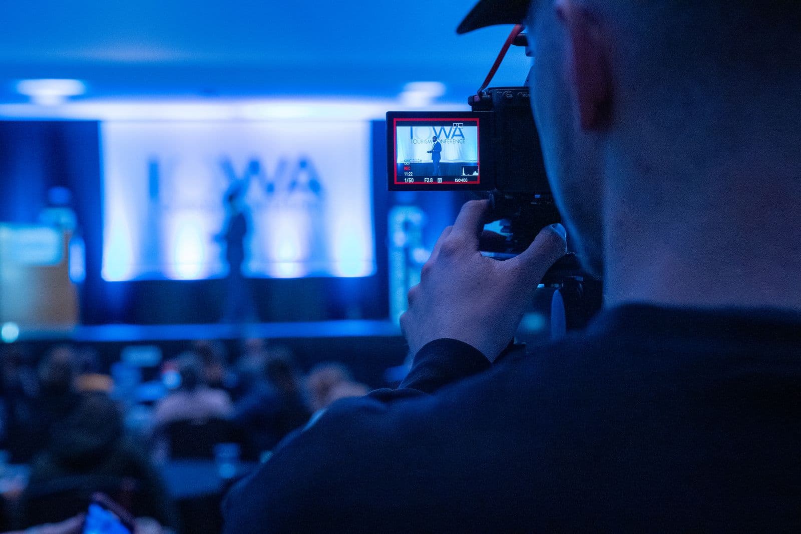 Camera operator recording a blue-lit corporate conference presentation